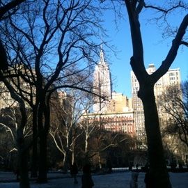 A New York City park in winter, the Empire State Building behind bare trees